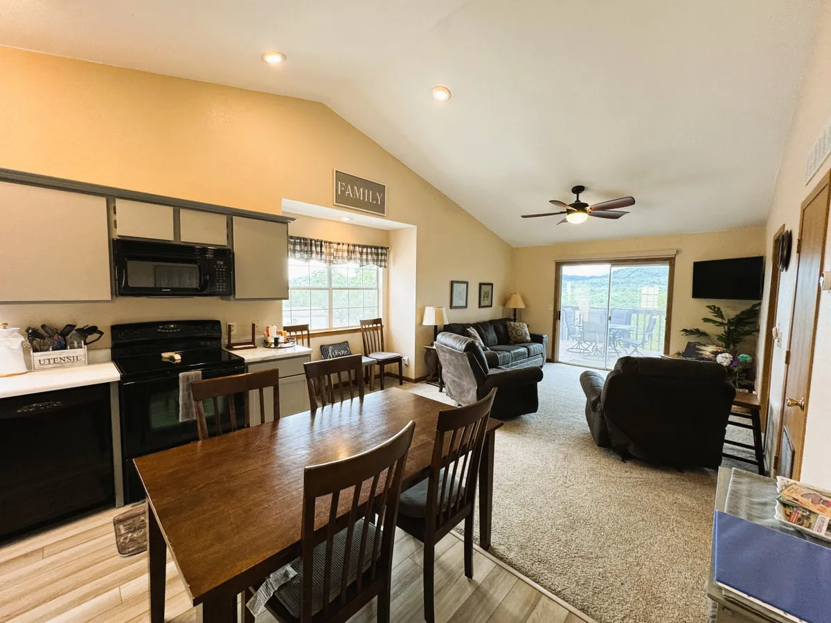 A warm, welcoming space where a dining table sits adjacent to a plush sofa, with a visible kitchen area and large window letting in ample natural light. The 'family' sign and overall decor emphasize a sense of togetherness and relaxation.