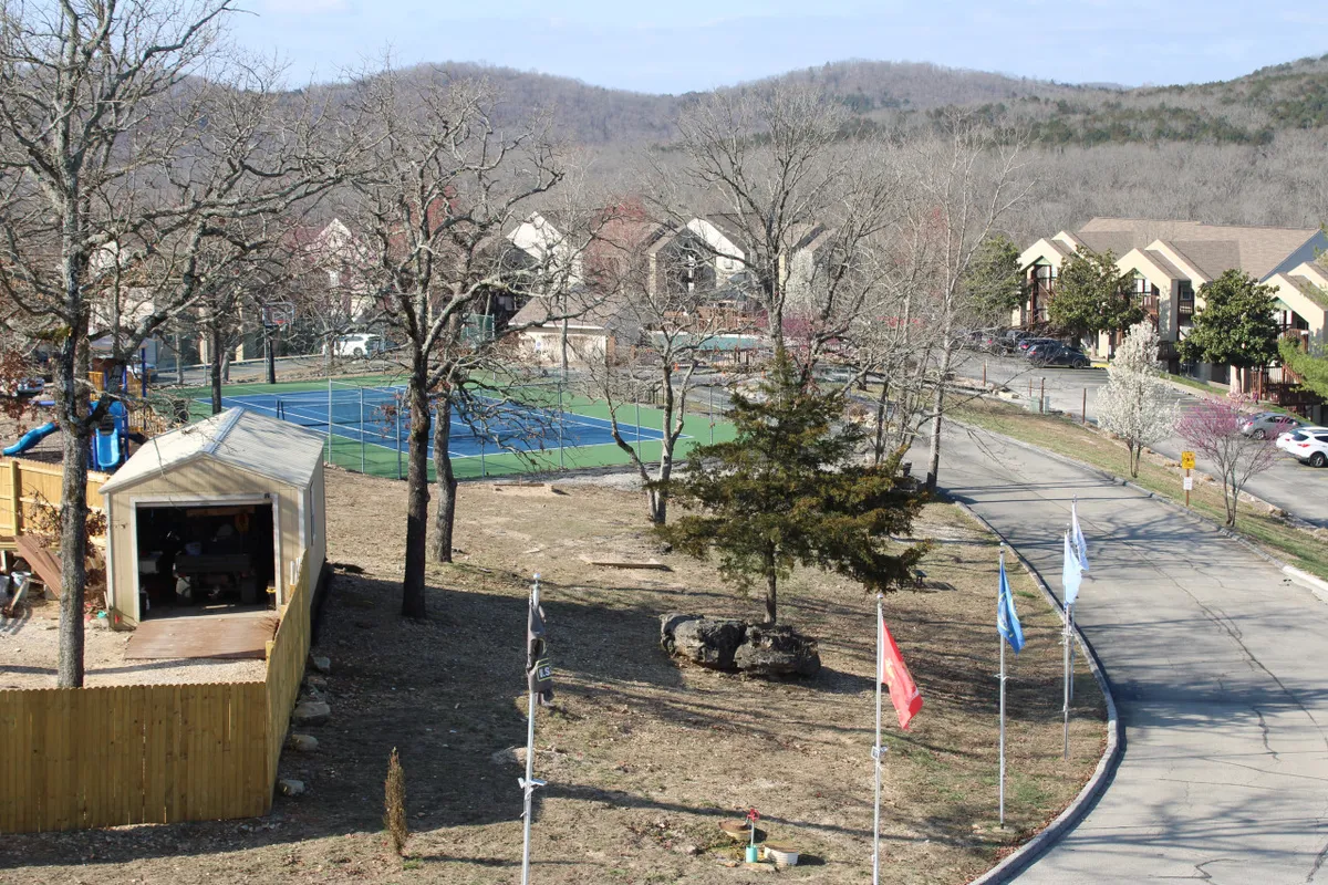 A lively exterior scene showcasing tennis courts and a playground structure surrounded by trees and nearby buildings. The area buzzes with potential for family play, sports, and outdoor gatherings, encapsulating the community’s active side.
