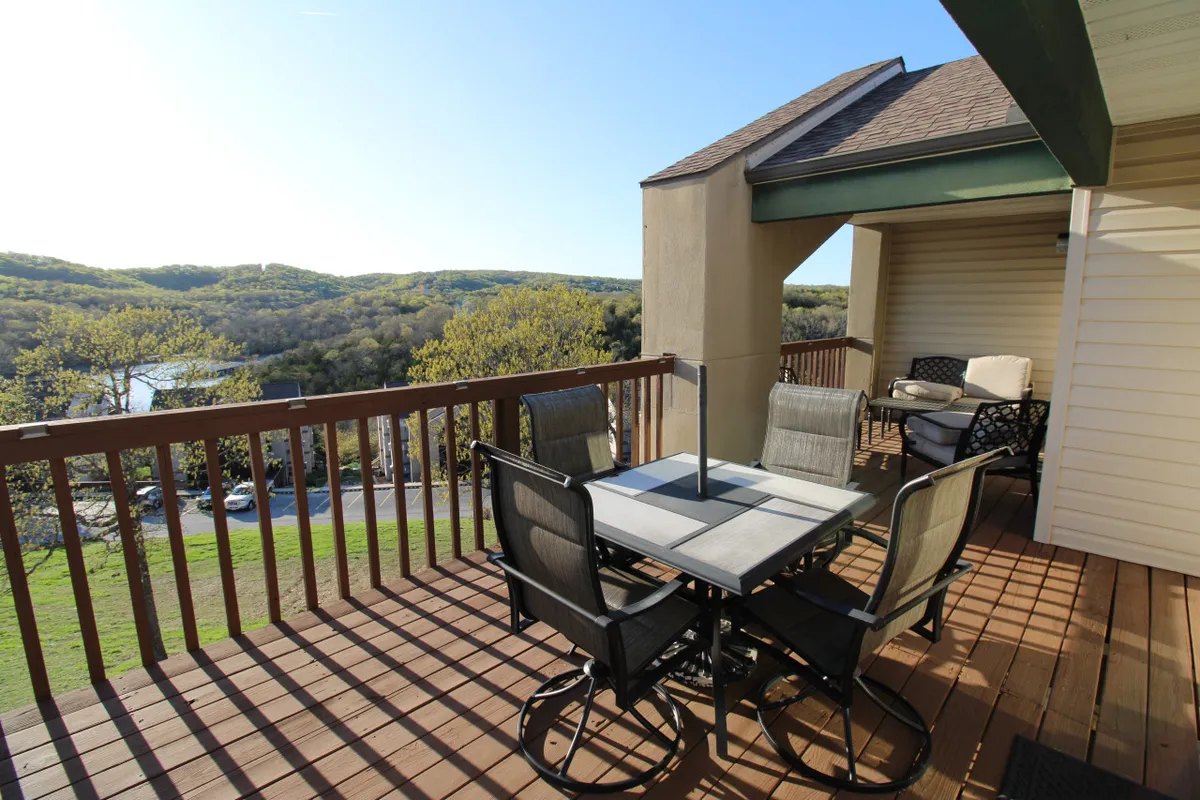 An inviting exterior deck setup featuring a dining table and lounge chairs, surrounded by lush greenery and open sky. The scene exudes tranquility and offers ample space for morning coffee, relaxation, or gathering with friends, all with the serene backdrop of nature.