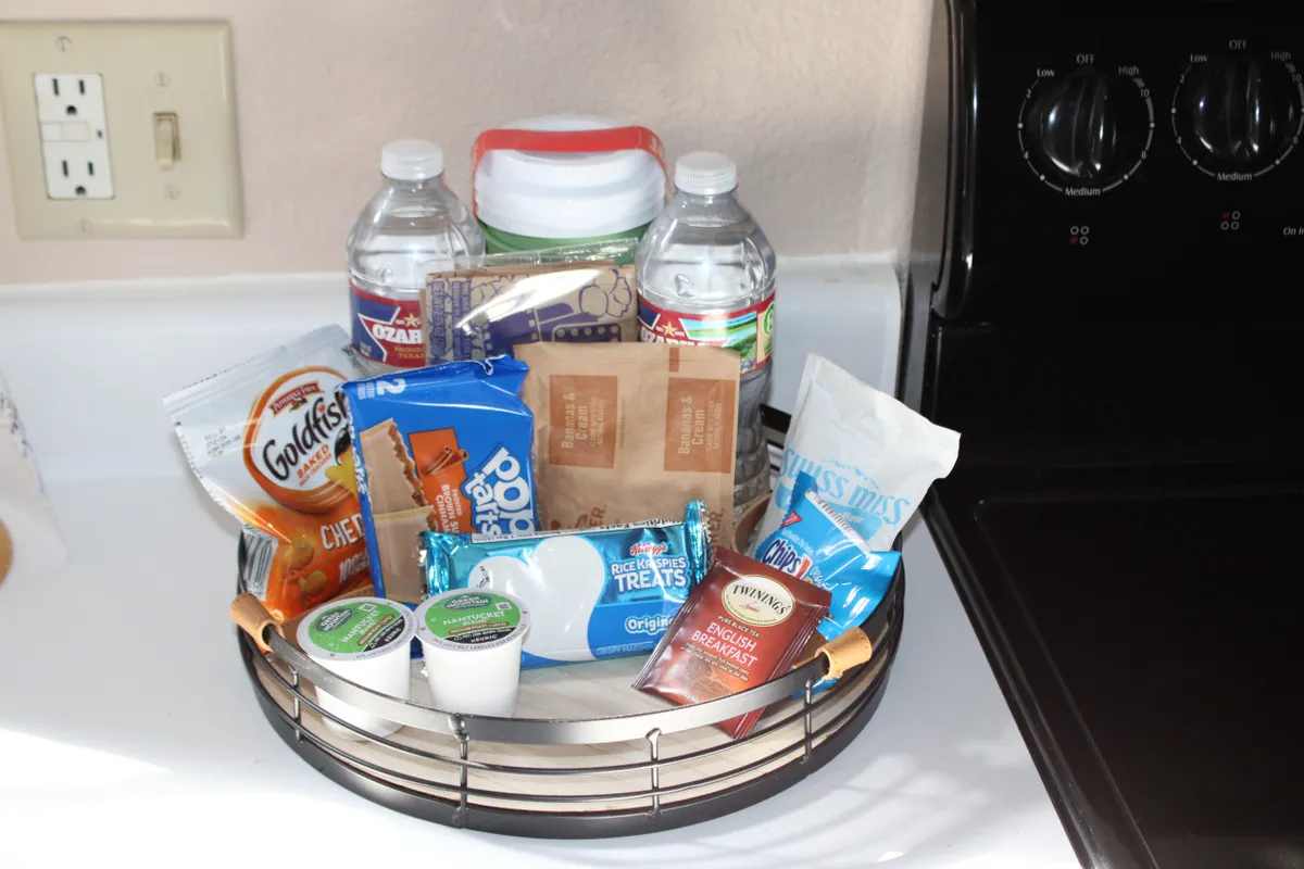 A close-up view of a basket of snacks, water bottles, and coffee containers neatly arranged, suggesting a welcoming atmosphere for quick breakfasts, impromptu snack breaks, or casual refreshments while preparing meals.