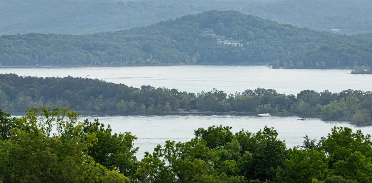 A serene view of Table Rock Lake surrounded by lush greenery and rolling hills, with hints of boating, fishing, and hiking activities. The calm waters reflect the setting sun, and the scene conveys tranquility and opportunities for outdoor recreation.