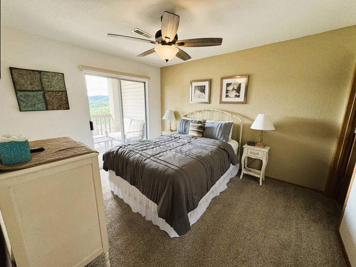 This image shows a tranquil bedroom with a bed positioned near a large window, accompanied by soft lighting from a bedside lamp, nightstand, and tasteful artwork on the wall. The overall mood is restful and inviting, emphasizing comfort and relaxation.