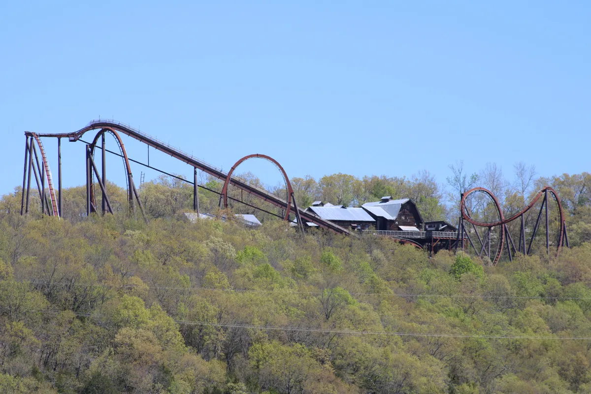The image showcases a thrilling wooden roller coaster set amidst lush trees, with an inviting family-friendly atmosphere perfect for adventure and creating lasting memories. The vantage point hints at spectacular hilltop views and proximity to Silver Dollar City, emphasizing outdoor excitement and togetherness.
