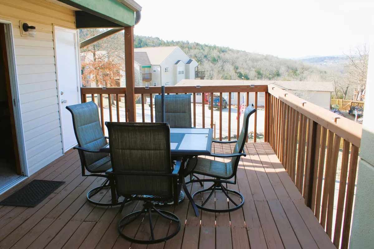 A spacious wooden deck featuring a stylish outdoor dining set overlooks a tranquil expanse of water and lush greenery. The area is bathed in soft, natural light and offers sweeping views of the lake, creating an inviting space for morning coffee or evening gatherings.